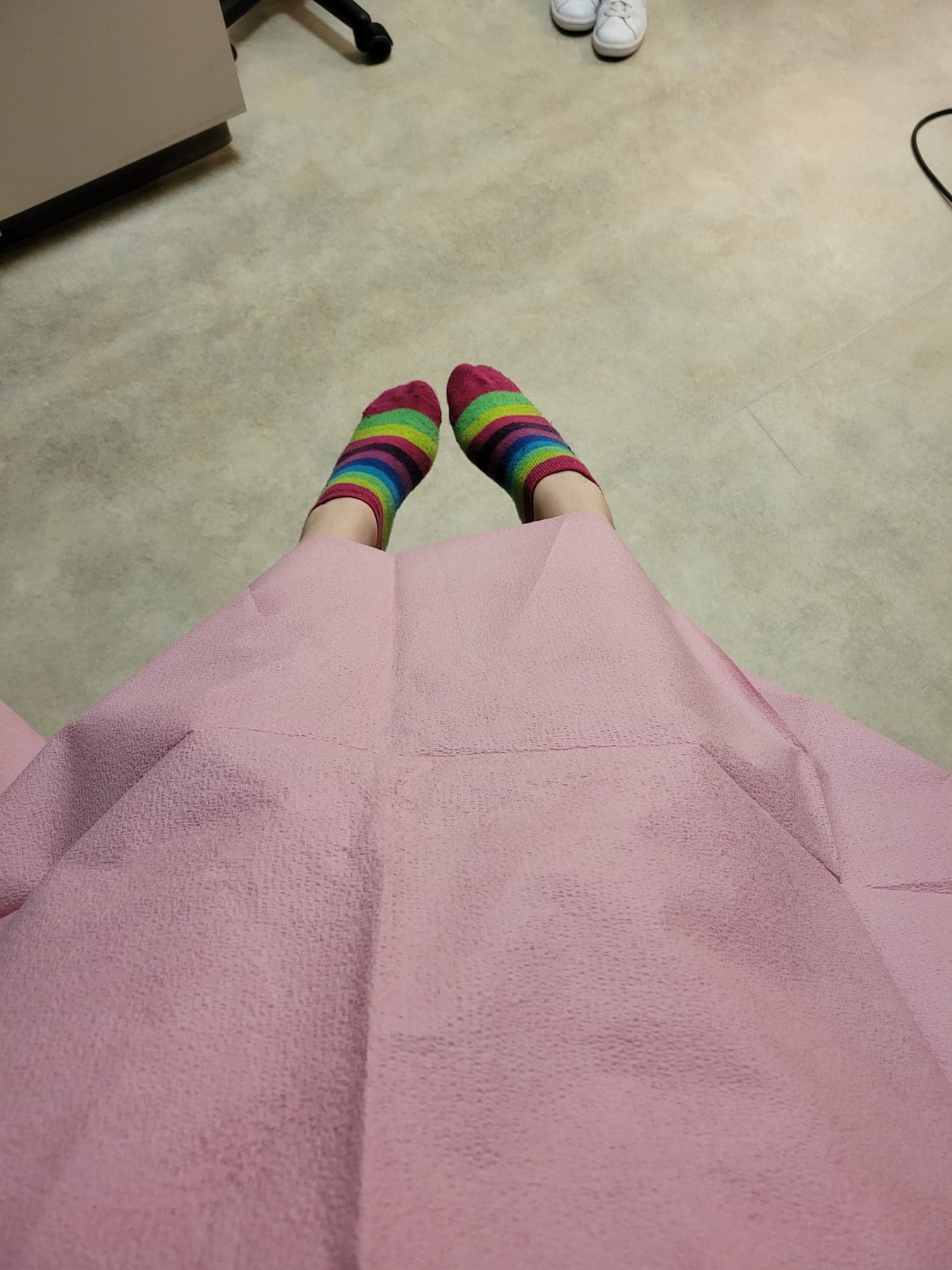 Legs in bright striped socks resting on a pink gown, waiting.